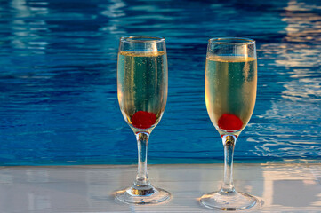Two wine glasses, with burrowing champagne and cherries, are isolated against the background of water. Big plan. Romantic background with the ability to insert text. Holidays, holidays. Travel. Annive