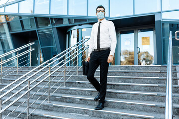 young businessman in business clothes, a man in a medical protective mask on his face, leaves the office building after a working day, Quarantine, coronavirus