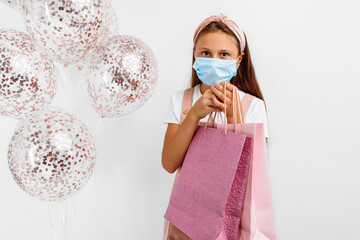 Smiling little girl wearing a medical protective mask on her face celebrating her birthday with...