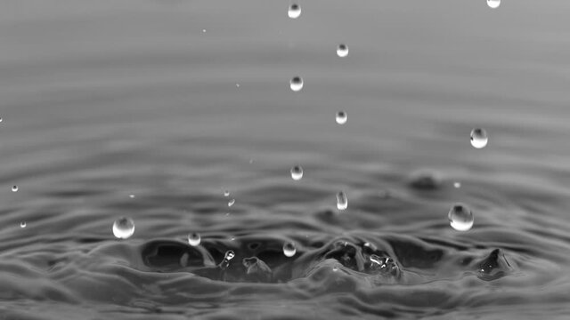 Super Slow Motion Shot of Water Drops Falling into Water on Black Background at 1000 fps.
