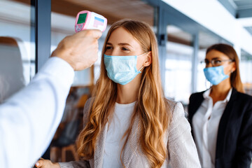 man with a non-contact thermometer measures the temperature of employees in protective masks at the entrance to a modern office, coronavirus, quarantine