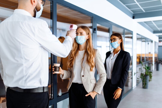 man with a non-contact thermometer measures the temperature of employees in protective masks at the entrance to a modern office, coronavirus, quarantine - Powered by Adobe