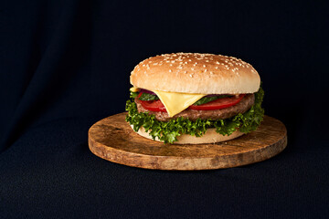 Delicious classic burger on wooden cutting board isolated on black background