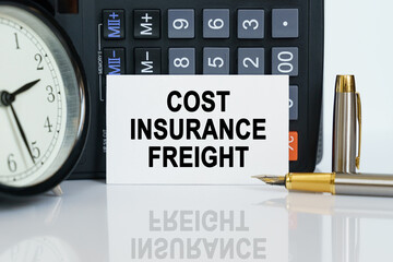 On the table there is a clock, a pen, a calculator and a business card on which the text is written - COST INSURANCE FREIGHT