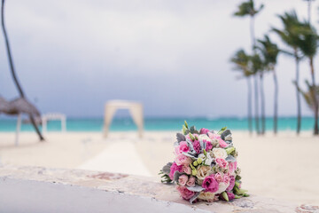 Close up view of bridal bouquet with colorful flowers and wedding gazebo at the background on the paradise beach with palm trees and blue water of Caribbean Sea, Punta Cana, Dominican Republic