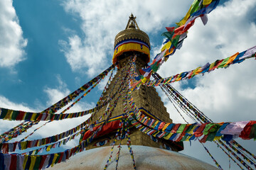 The upper part of the Boudhanath stupa in Kathmandu, Nepal. The image of Buddhas eyes on a gold surface of the stupa. Colorful prayer flags nearby.