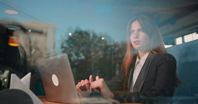 A successful business woman is sitting and working on a laptop computer in cafe, typing text. She looks thoughtfully out the window. Suddenly finds a desicion. H.264. 4k.