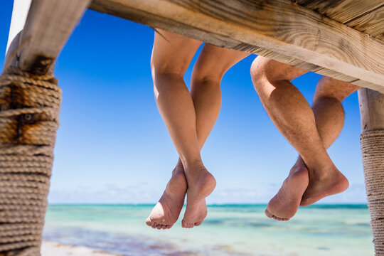 Close up view of legs of couple woman and man hanging from the wooden pier over the blue water of Caribbean Sea, Punta Cana, Dominican Republic 