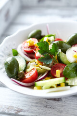 Healthy Salad with Green Olives, Baby Spinach, Cucumber, Cherry Tomatoes and Capers. Bright wooden background. Close up.	
