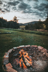 Campsite With Fire Pit. Burning Campfire with mountain landscape with evening sunset sky over the forest and hills.
