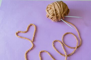 Top view. Brown knitting yarn. Knitting needles stuck in yarn. Empty space for text and add. Heart laid out of yarn. 
