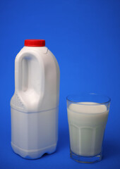 Airtight one gallon milk jug with a red cap and full glass milk on blue background