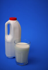 Airtight one gallon milk jug with a red cap and full glass milk on blue background