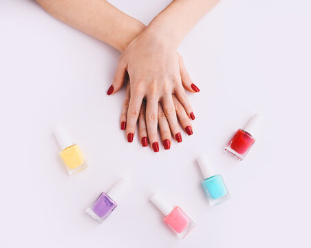 Nail Polish. Art Manicure. Multi-colored Nail Polish Bottles around female hands with stylish red nails