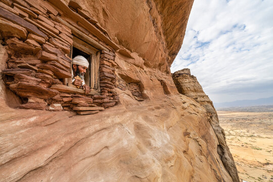Priest looking out from a small window carved into rocks in Abuna Yemata Guh church, Gheralta Mountains, Tigray Region, Ethiopia