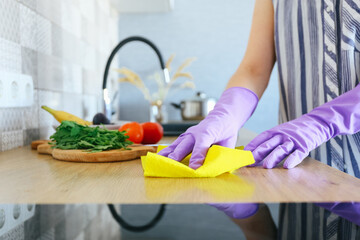 Woman in protective gloves cleaning kitchen table with rag