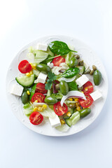 Healthy Salad with Feta Cheese, Green Olives, Baby Spinach, Cucumber, Cherry Tomatoes and Capers. Bright background. Top view. 