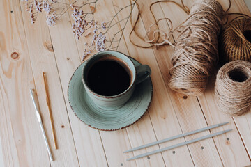 Top view. Yarn for knitting and crocheting. Knitting needles stuck in yarn. Different types of crochet hooks. Next to it is a green cup on a saucer with coffee. On a wooden background. Hobby concept.