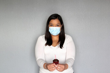 latin woman with black hair with protection mask, celebrates birthday with cake at home due to...