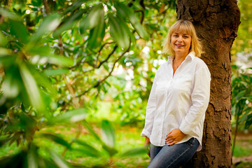 A beautiful woman,blonde,middle-aged,in a white shirt stands near a tree, in a Park,on a beautiful autumn day