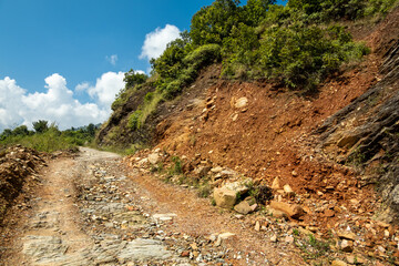 An old rocky dirt road in the mountains with traces of a recent landslide on the nearby side of the gorge.
