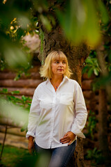 A beautiful woman,blonde,middle-aged,in a white shirt stands near a tree, in a Park,on a beautiful autumn day