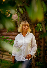 A beautiful woman,blonde,middle-aged,in a white shirt stands near a tree, in a Park,on a beautiful autumn day