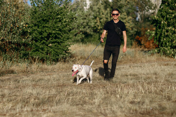 Young stylish man walks with his dog in the park, white staff terrier for a walk