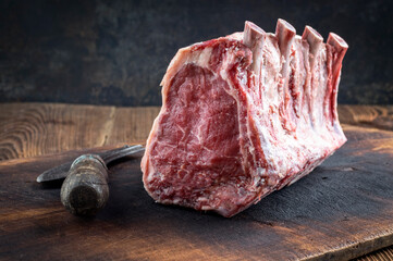 Raw dry aged angus cote de boeuf block offered as closeup on a rustic wooden cutting board