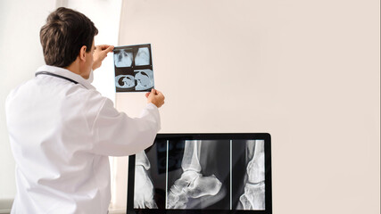 Back view of young man radiologist doctor holding and analysis x-ray and computed tomography film in his xray room from a hospital.