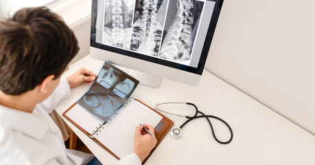 Top view of young man radiologist doctor analises x ray and computer tomography film and make a...