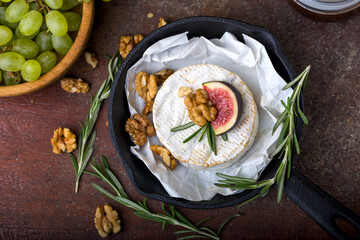 Camembert cheese in cast iron pan, on paper, pelled walnuts, sprigs of rosemary, green grapes....