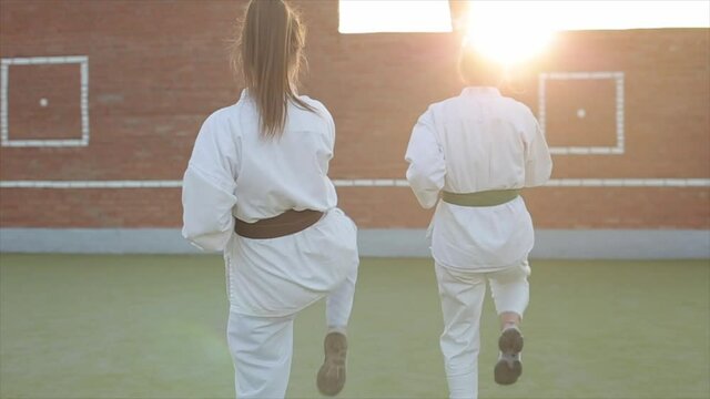 Young female athletes in karate training work out of techniques of defense and attack against the backdrop of a sunset. Front view. Close-up