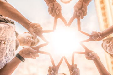 Bottom view in focus four pairs of hands showing sign V - victory on the sky background.