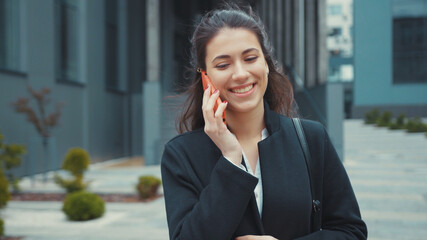 Appealing office young woman walking outside of building using smartphone app networking getting messages on social media smiling cheerful and relaxed.