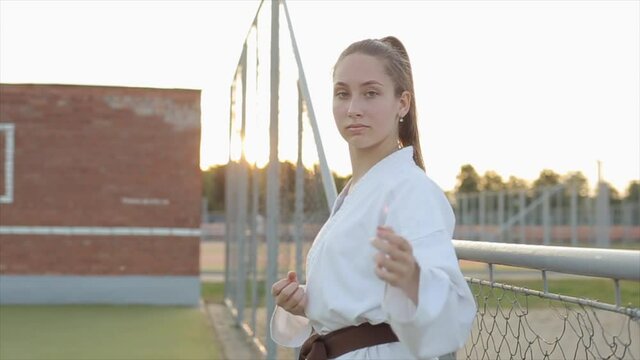 A karate girl in training on the sports ground demonstrates the movement of her hands using the Kyokushinkai technique. Front view. Close-up. Slow motion