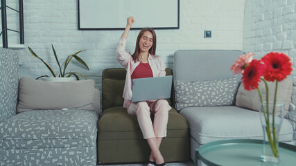 Cheerful young woman worker learns great news on laptop clapping hands to celebrate business...