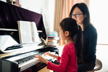 mother teaching daughter to play piano