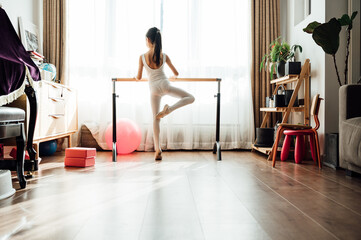 Portrait of cute little girl practicing ballet and standing at barre at home