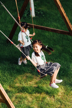Cute little girls playing swing in garden