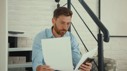 Fototapeta premium Unhappy businessman working with smartphone and documents on sofa holds papers worried sad phone smartphone internet cell attractive slow motion