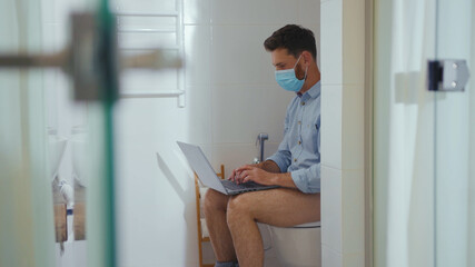 Happy businessman working on laptop wearing mask sit on the toilet at home restroom bearded funny wc isolation quarantine pandemic coronavirus covid-19 portrait close up slow motion