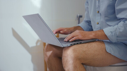 Sad businessman working on laptop wearing mask sit on the toilet at home restroom bearded serious wc isolation quarantine pandemic coronavirus covid-19 portrait close up slow motion