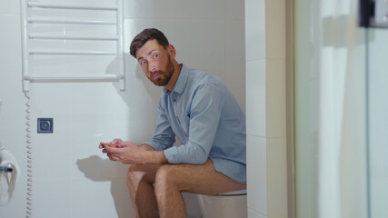 Happy businessman use phone sitting on the toilet smiling mobile restroom smartphone internet home bathroom close up slow motion