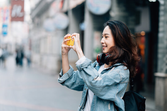 Young asian woman traveling in a city downtown and taking pictures with her cell phone