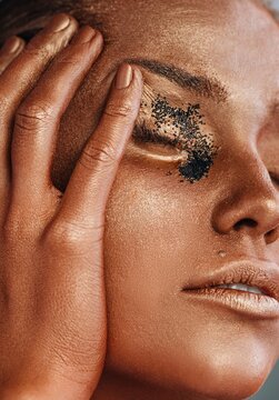 Crop model smearing paint and glitter on face