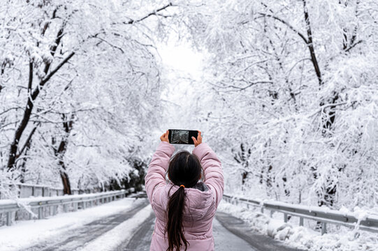 Cute little girl taking photos on a snowy forest road on a winter day