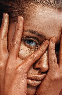 Bronzed model looking at camera through fingers