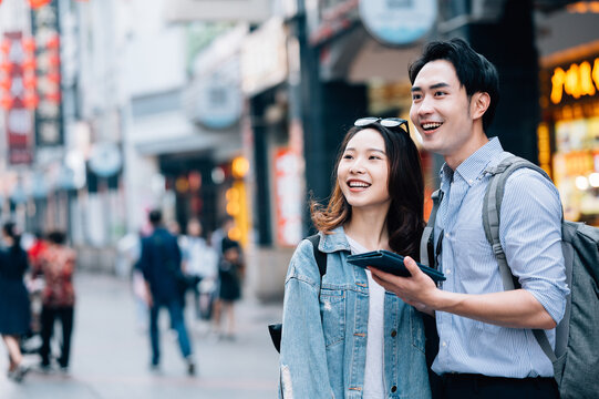 Young asian couple traveling in a city downtown and checking information on tablet