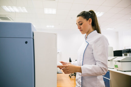 Side view of woman in lab coat holding samples while working in modern laboratory